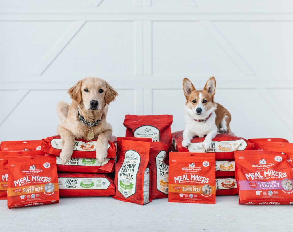 Two dogs sitting on a pile of dog food bags